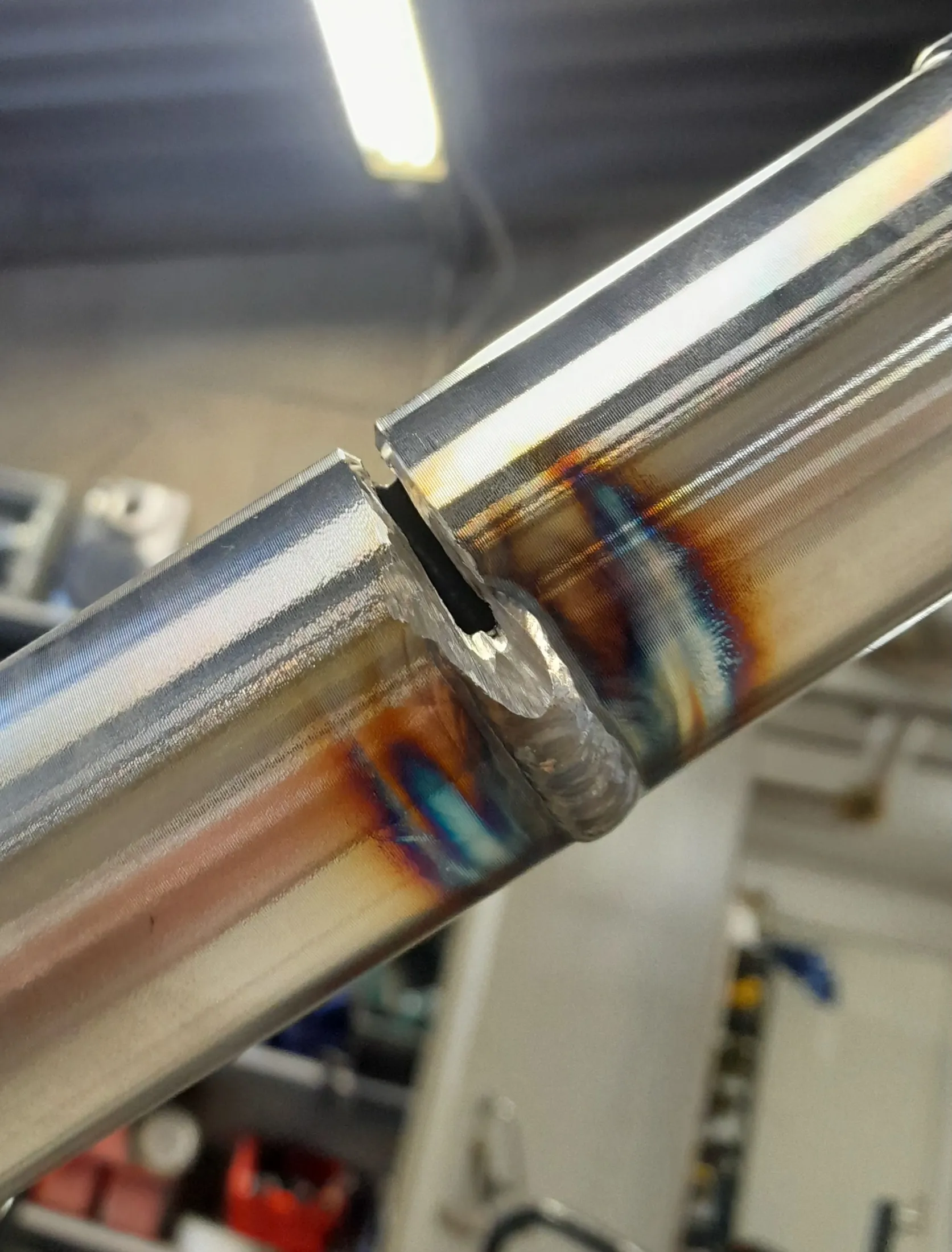 Lähikuva hitsatusta metalliputkesta, jossa näkyy hitsausjälki ja lämpövärit. Kirkas valo ylhäällä.