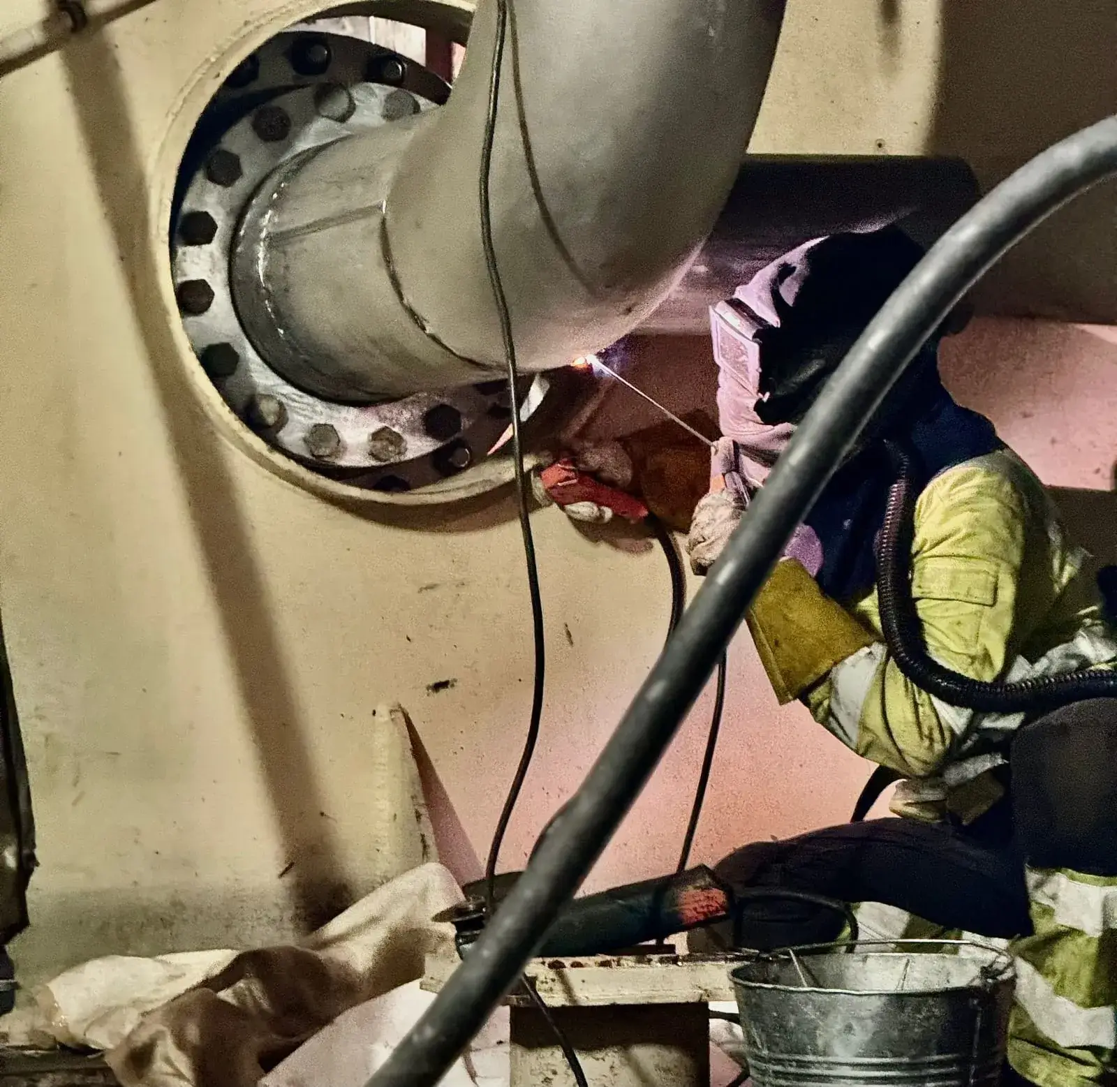 Hitsaaja hitsaa putkea suojavarusteissa, valoisa hitsausvalo, metalliputket ja -rakenteet.