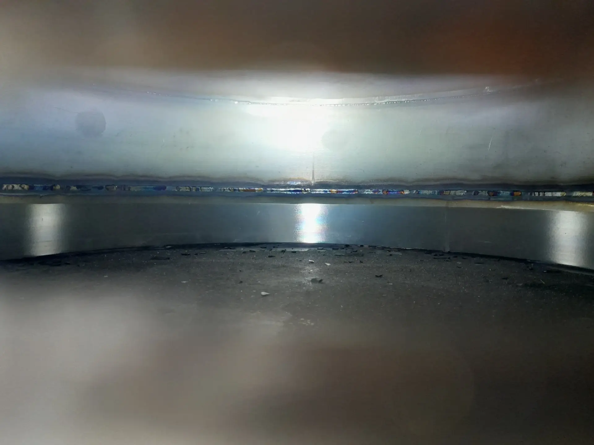 Metallinen sisäpinta, jossa hitsausjälkiä ja valoheijastuksia.