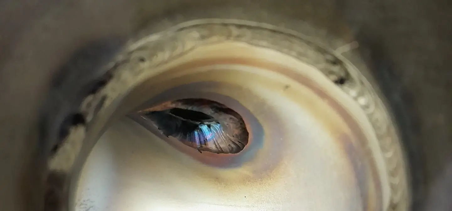 Lähikuva metallisesta, irisoivasta reiästä, jossa on sinisiä ja violetteja sävyjä, ja ympärillä on kiillotettu metallipinta.