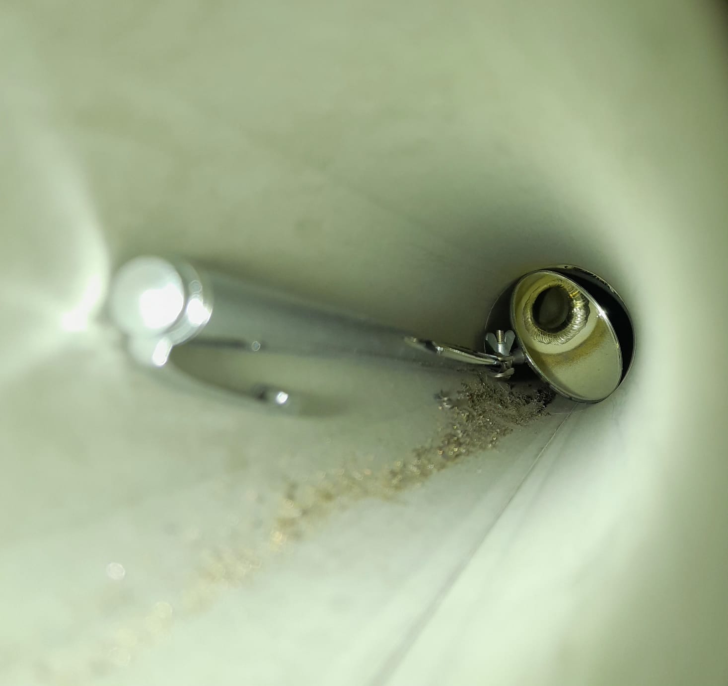 Metallinen suukappale ja hopeinen putki valkoisessa suppilossa, jossa on hiekkaa pohjalla, valaistus on kirkas.